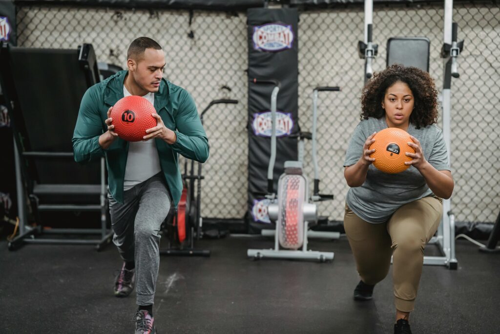 Two people engaging in a focused workout using medicine balls in an indoor gym setting.