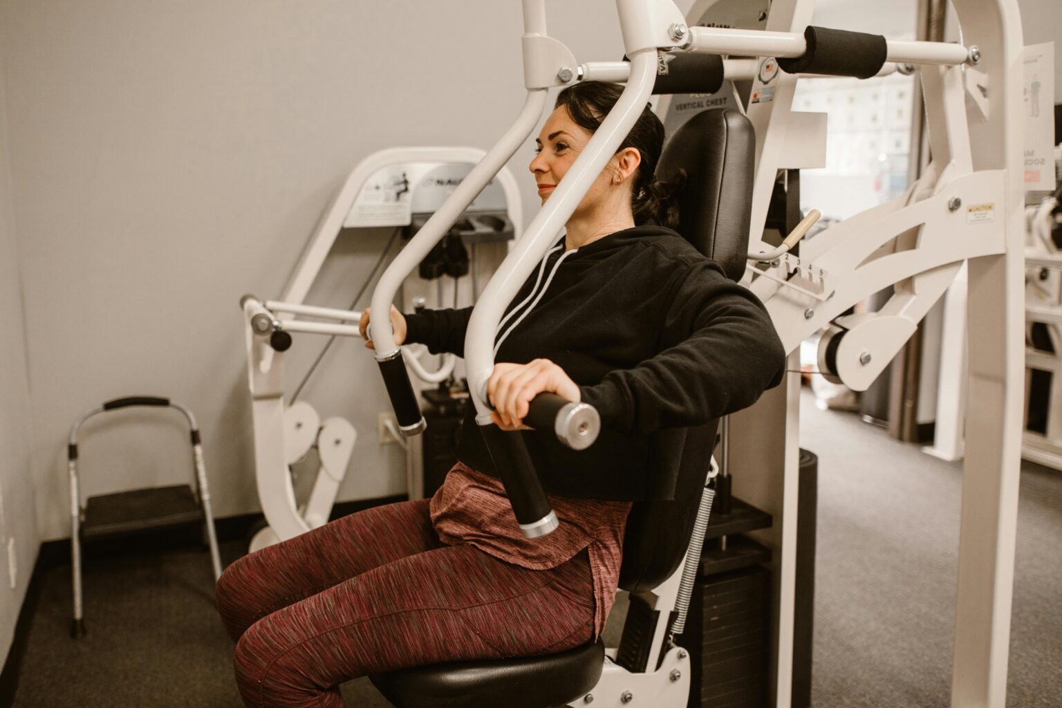 Woman working out on a chest press machine, promoting fitness and health in a gym setting.