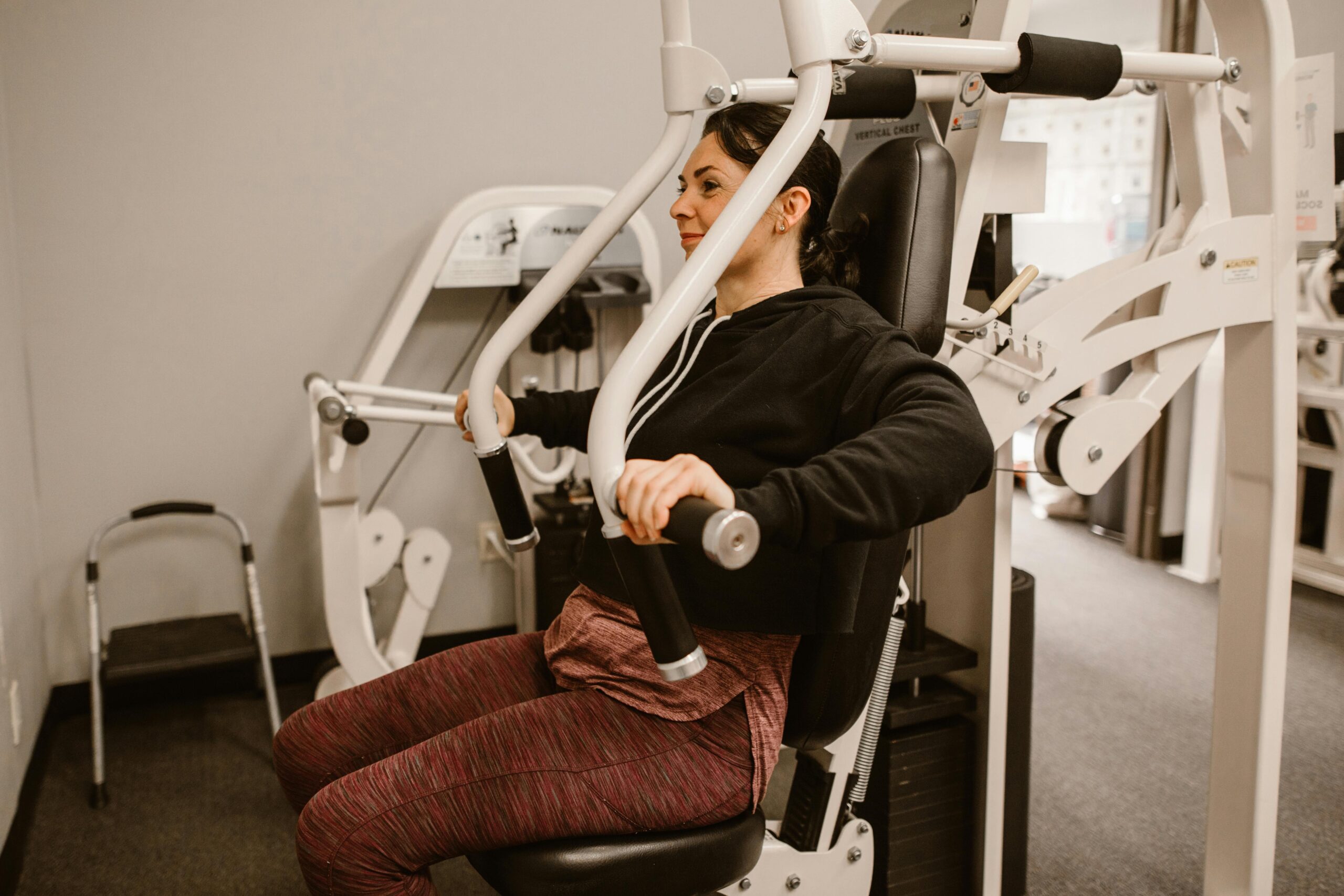Woman working out on a chest press machine, promoting fitness and health in a gym setting.