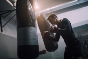 A male boxer intensely training with a punching bag in a well-lit boxing gym.