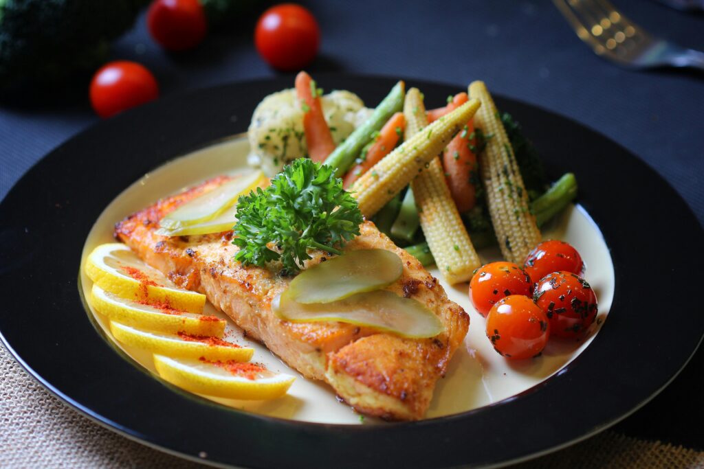 Deliciously plated salmon with cherry tomatoes, lemon slices, and assorted vegetables.